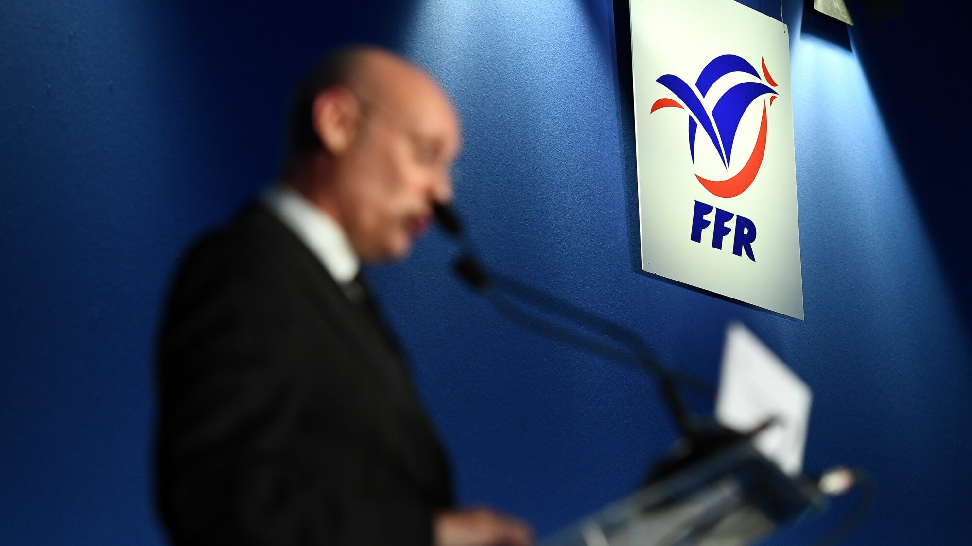 Le logo de la Fédération Française de Rugby, avec Bernard Laporte flou au premier plan