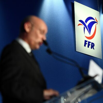 Le logo de la Fédération Française de Rugby, avec Bernard Laporte flou au premier plan